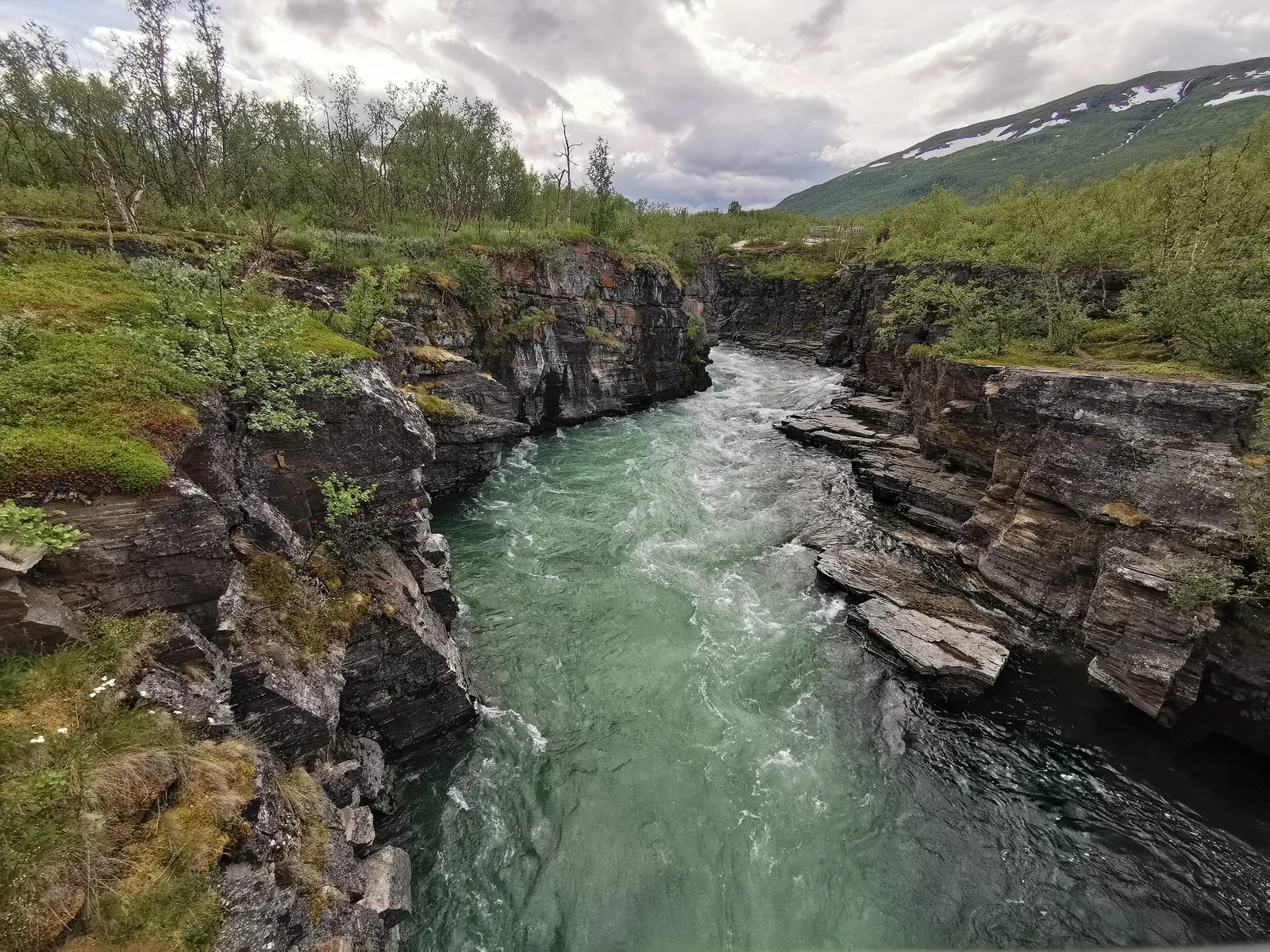 The turquoise Abiskojåkka flows through a narrow canyon of layered rock in Abisko National Park, with birch scrub along the edge
