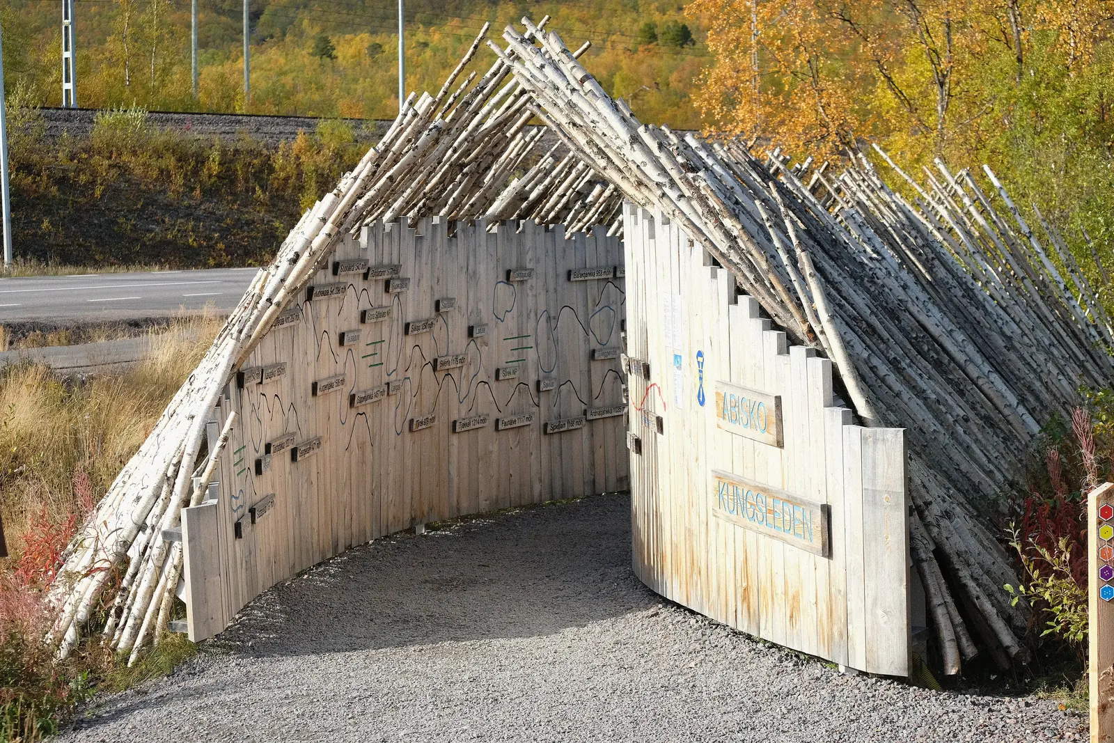 The wooden entrance gate inscribed Kungsleden at the start of the long-distance trail by Abisko Turiststation, surrounded by autumn birch leaves
