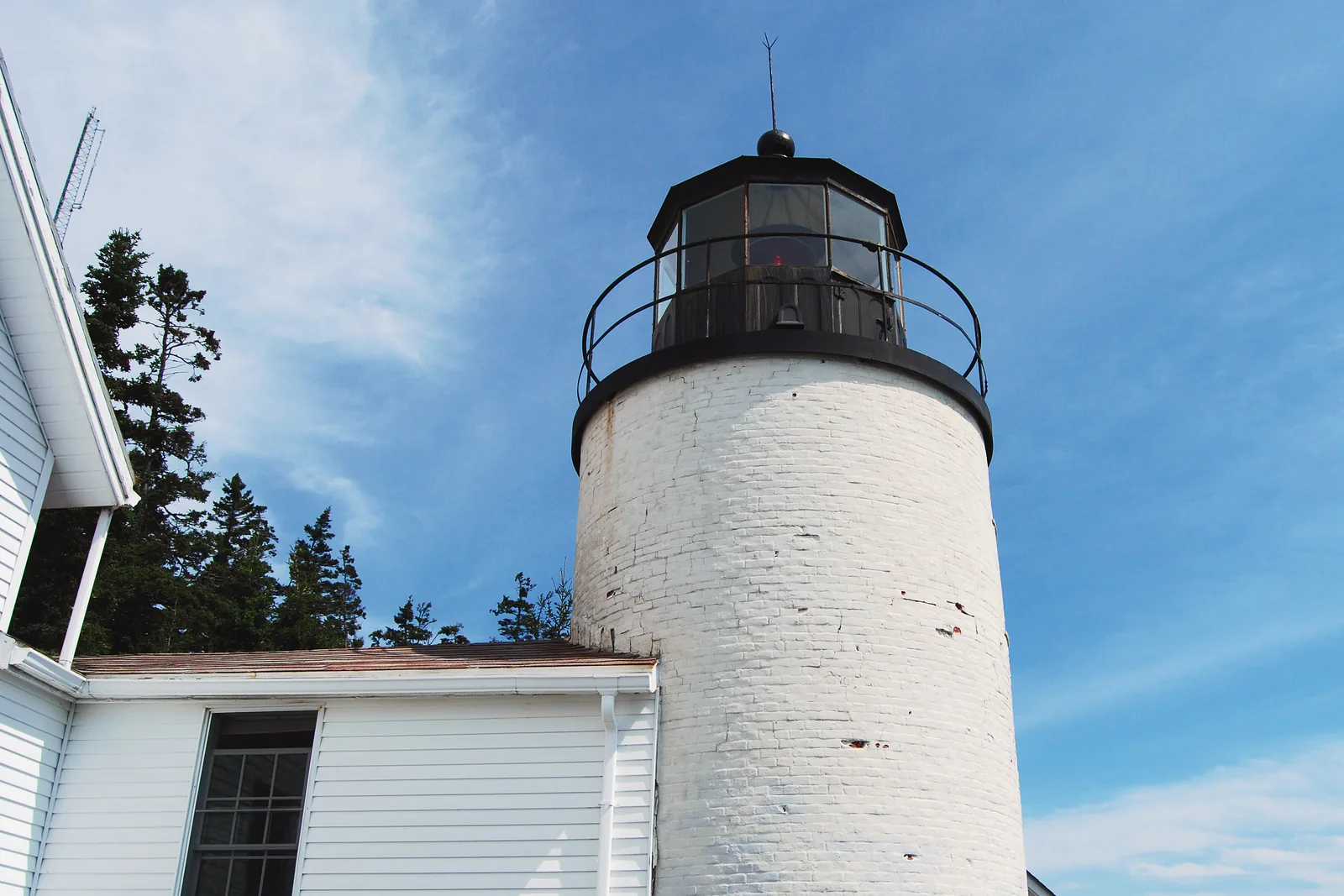 The white tower of Bass Harbor Head Light in Acadia National Park, with its black lantern against a blue sky, the keeper's house in front