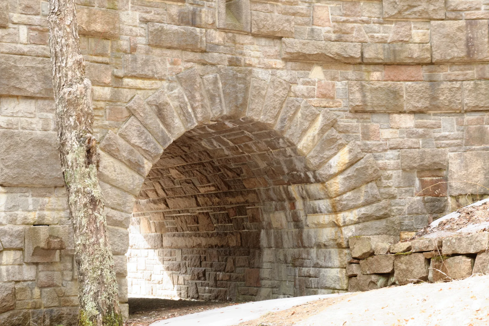 Stone arch bridge of pink granite blocks over a carriage road section in Acadia National Park