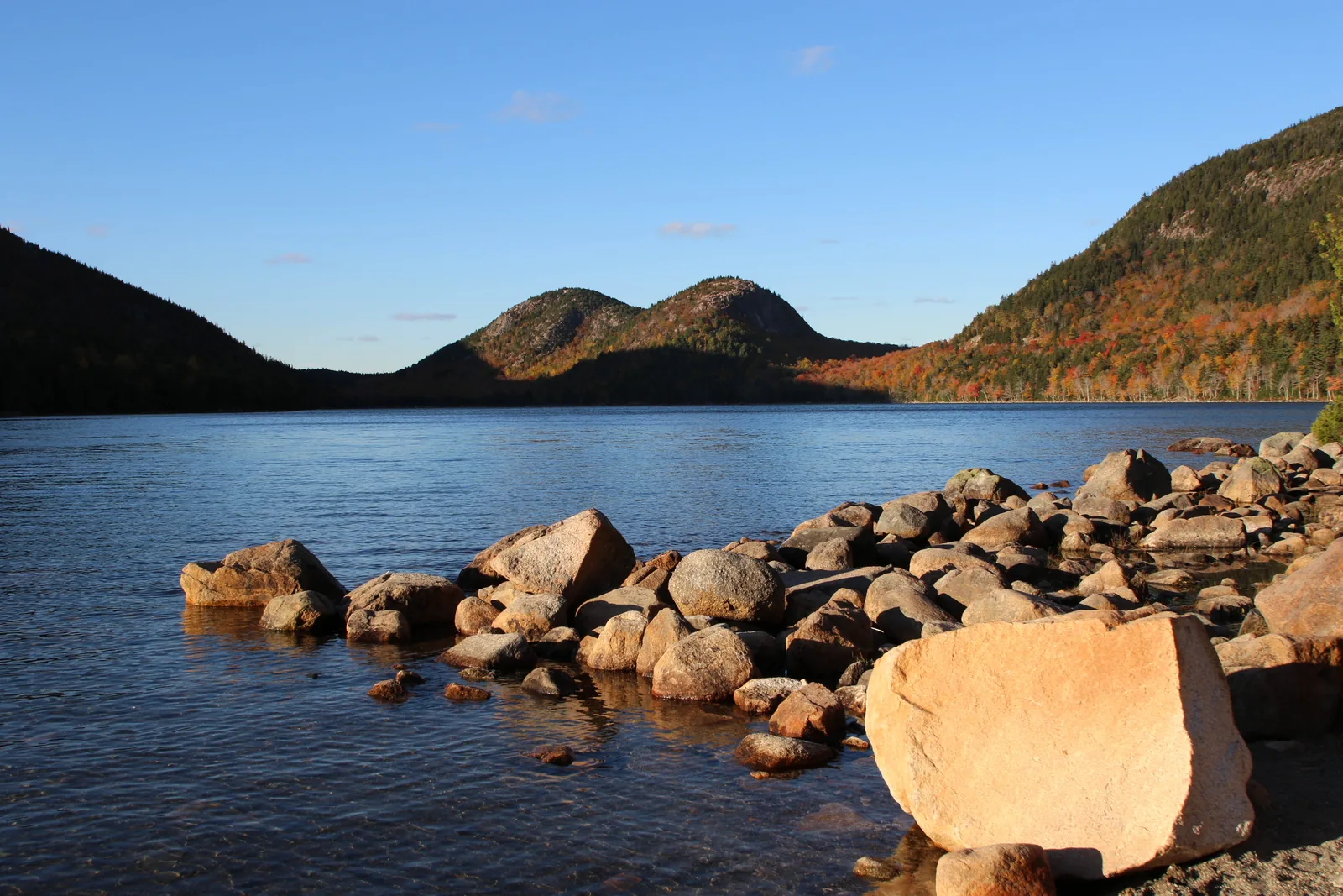 Jordan Pond in Acadia National Park in evening light, pink granite boulders on the shore and the two rounded summits of the Bubbles behind