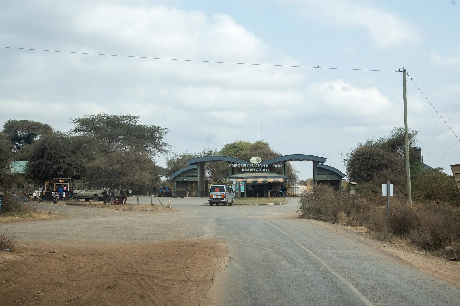 The access road to Kimana Gate of Amboseli National Park, with the gate building between acacias at the end of the road