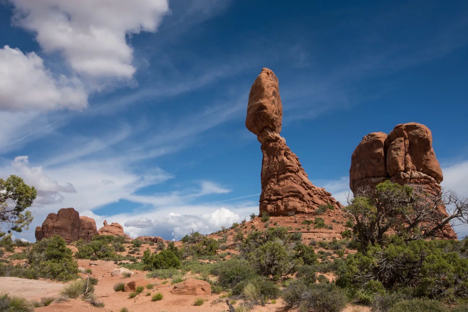 A large boulder in Arches National Park on a narrower base against a blue sky with wispy clouds