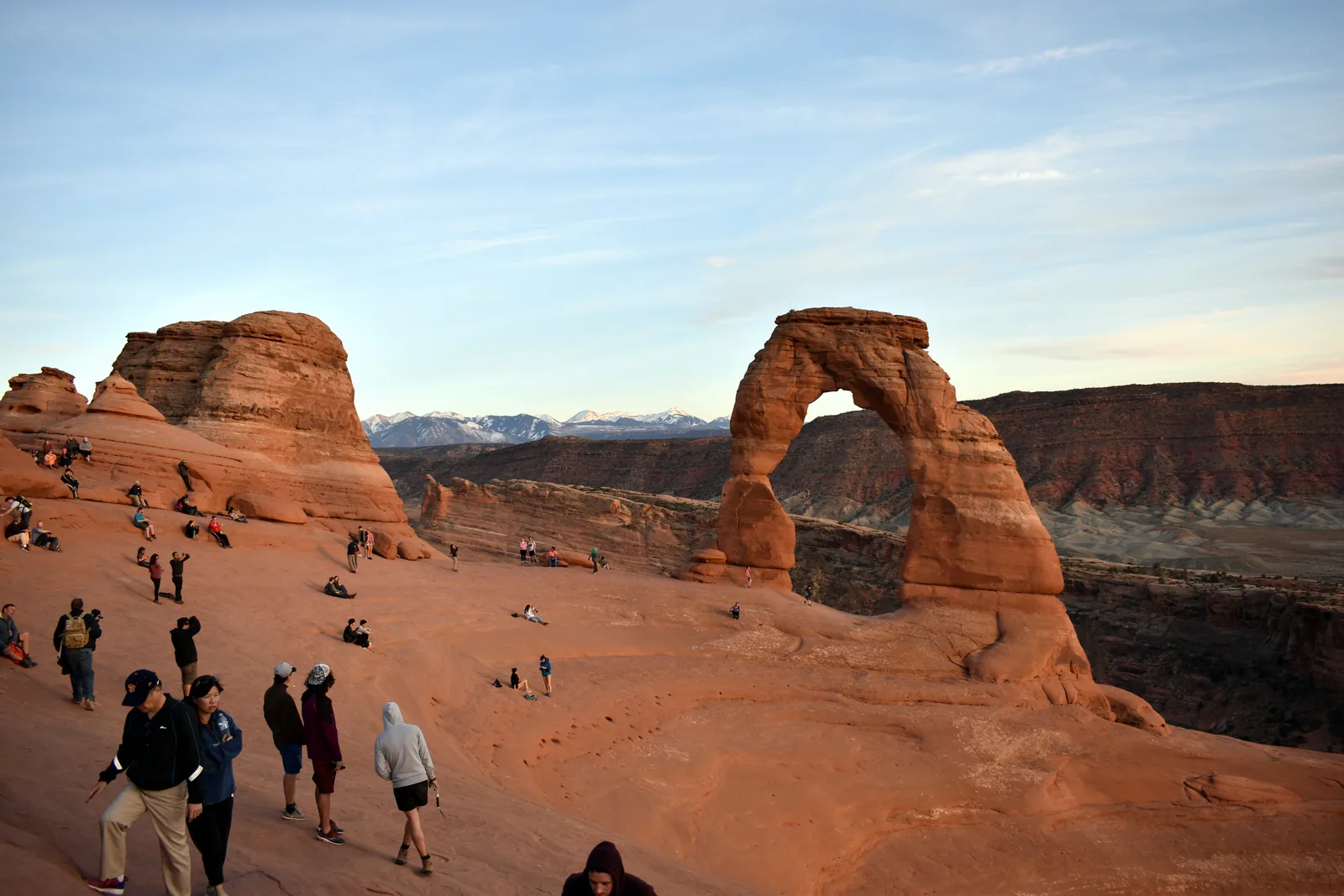 Dozens of people sit and stand in the rock bowl in front of Delicate Arch in Arches National Park, waiting for the sunset