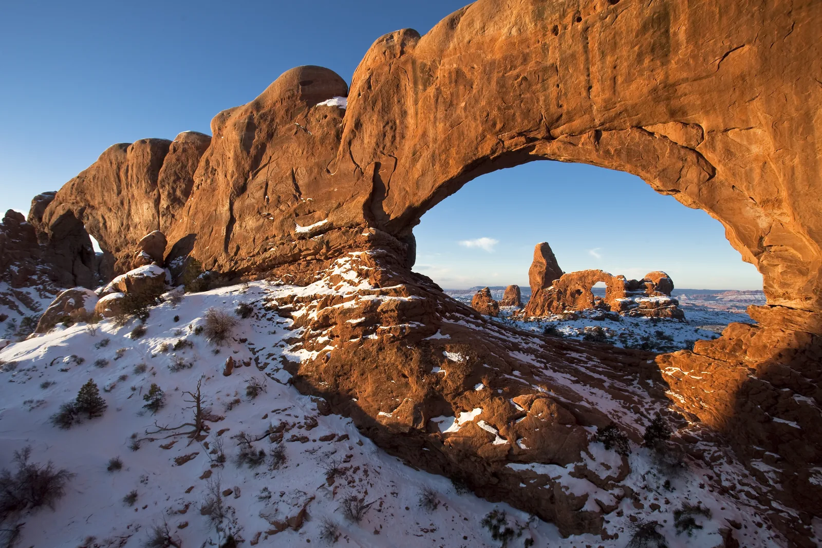 Turret Arch in Arches National Park, framed by the opening of North Window in the first morning light, above snow-covered ground