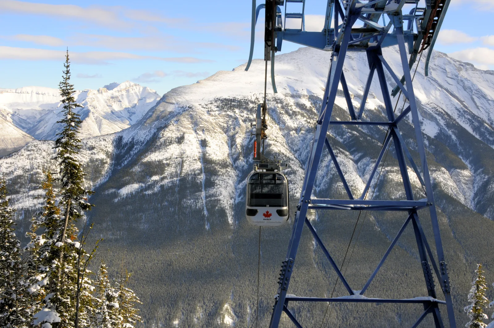 Gondola cabin in Banff National Park with a maple leaf on a blue steel tower in front of snowy mountains.