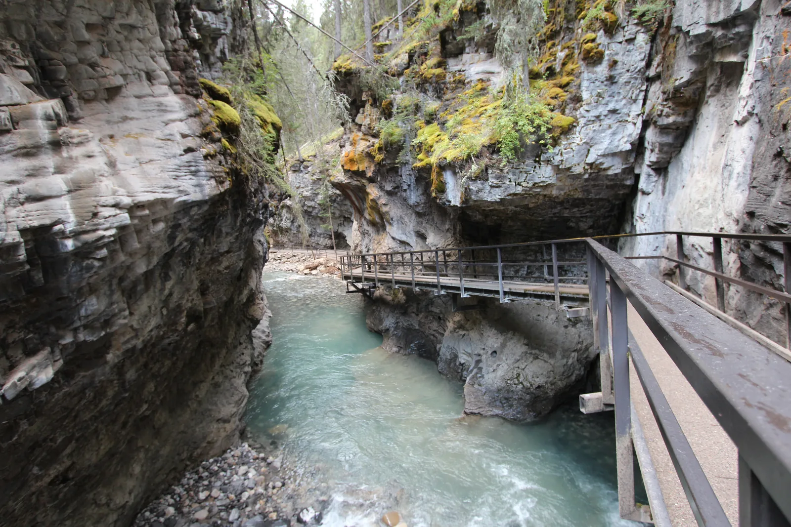 Metal catwalk with railing in Banff National Park on the rock wall of Johnston Canyon above the turquoise creek.