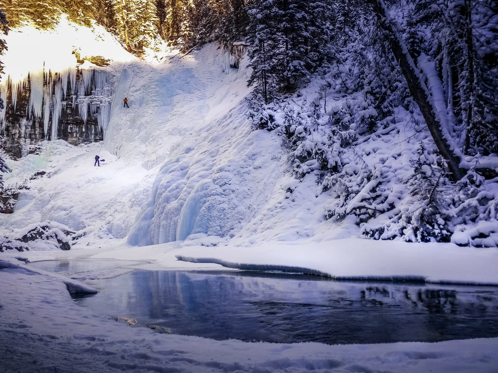 Frozen waterfall in Johnston Canyon in Banff National Park with ice climbers, a snowy creek in front.