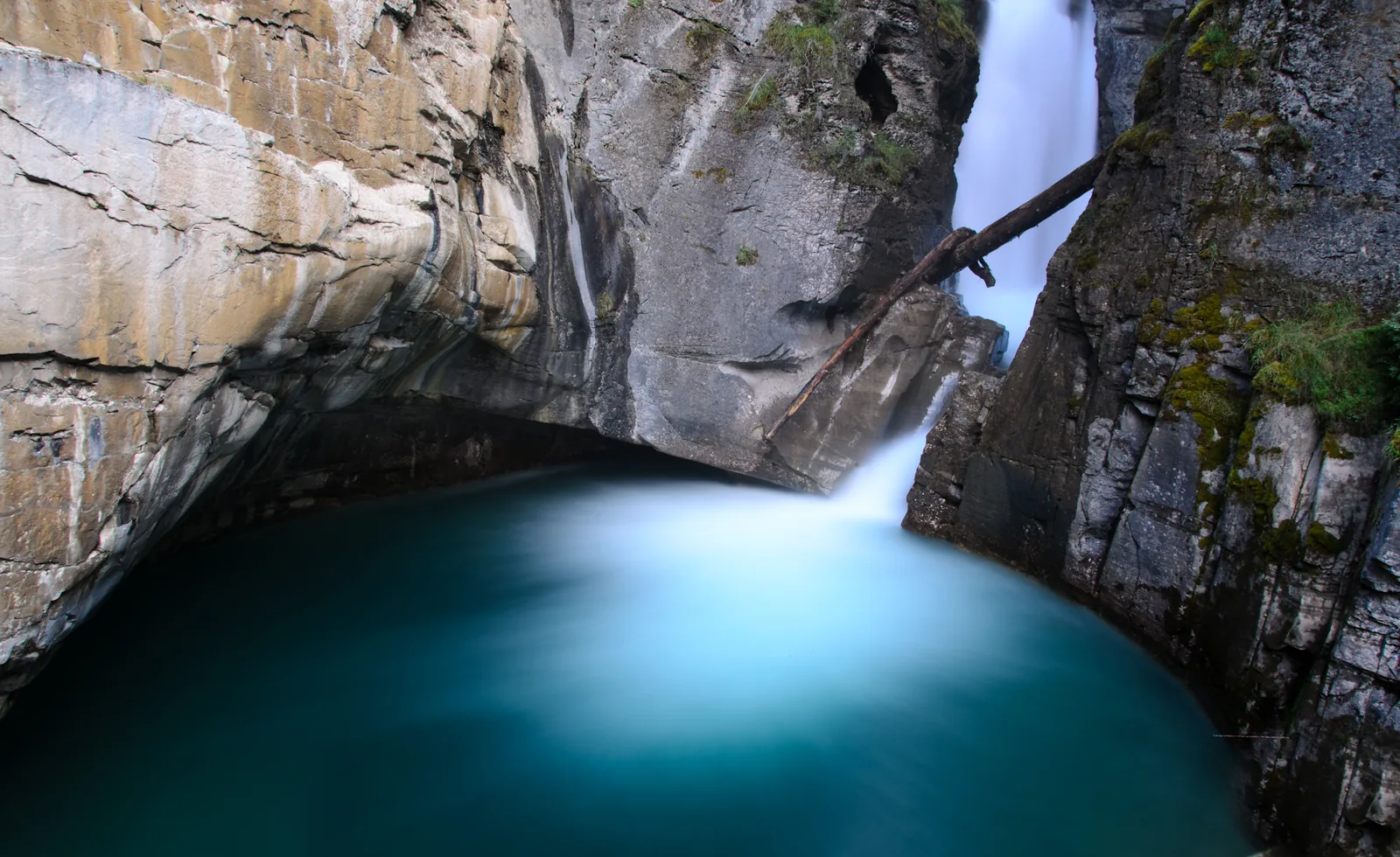 The Lower Falls in Johnston Canyon in Banff National Park plunge into a turquoise pool below the rock wall.