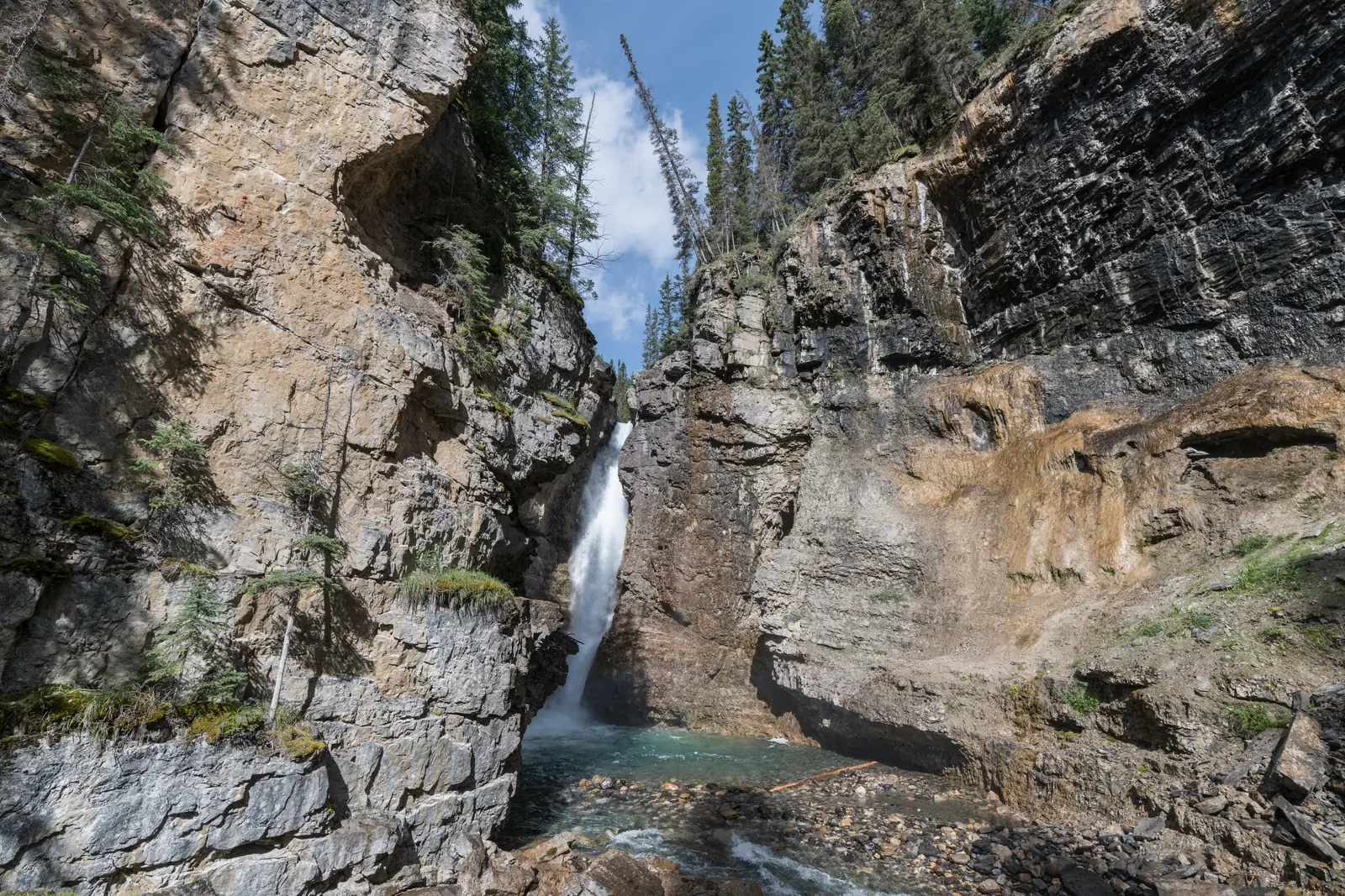 The Upper Falls in Johnston Canyon in Banff National Park between high limestone walls, seen from the viewpoint at the base.