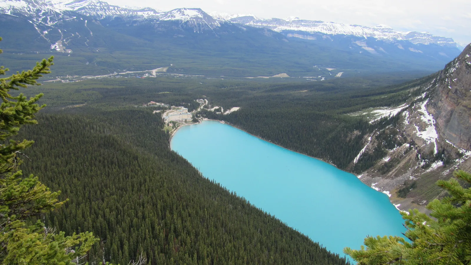 View from above in Banff National Park of turquoise Lake Louise between forests, the hotel at the far end.