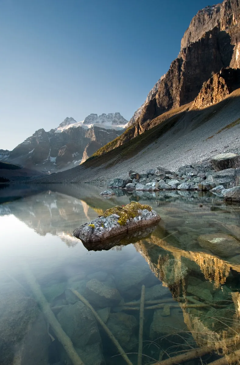 Still water of Lower Consolation Lake in Banff National Park with rocks and a reflected mountainside.