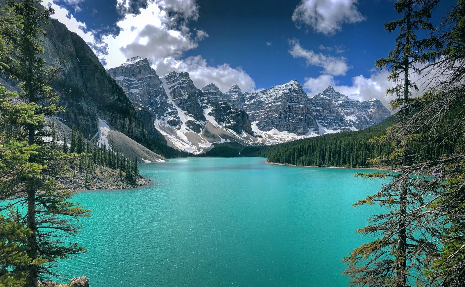 Turquoise water of Moraine Lake in Banff National Park below forested and snow-capped mountains.