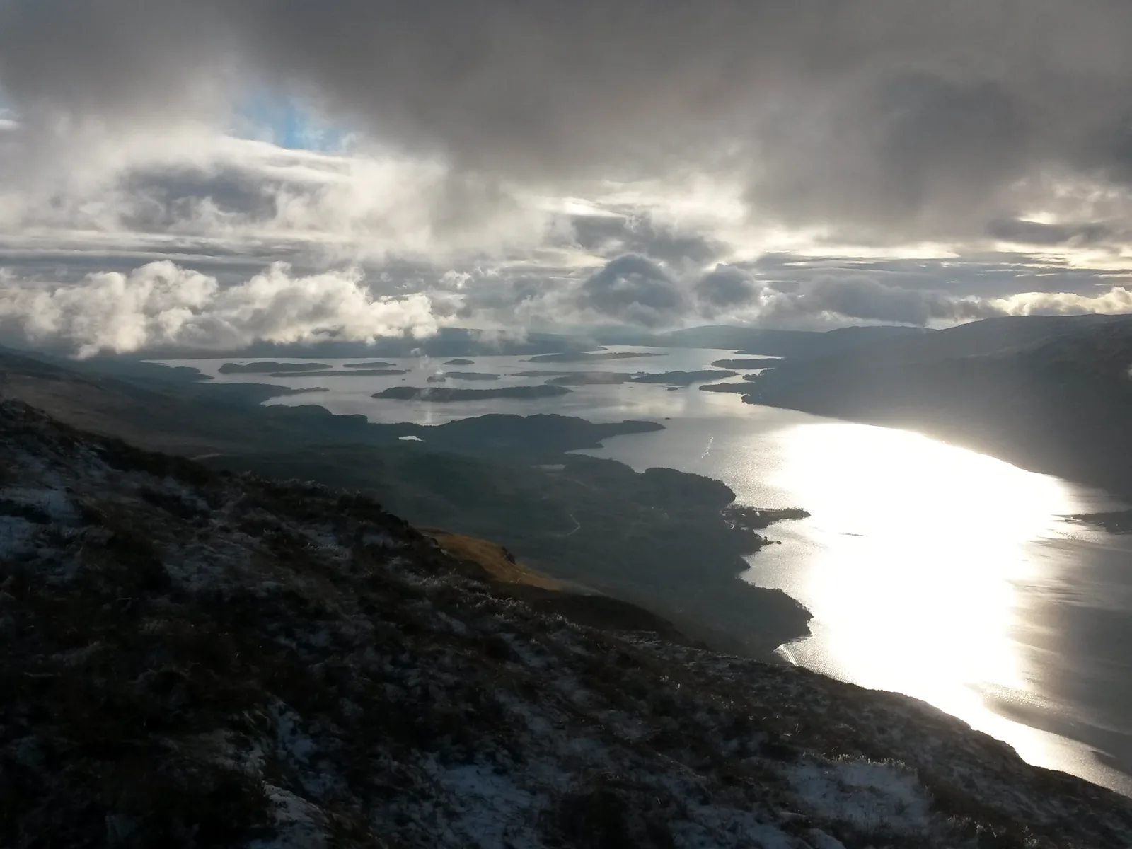 View from the slopes of Ben Lomond in Loch Lomond & The Trossachs National Park to sunlit Loch Lomond under clouds