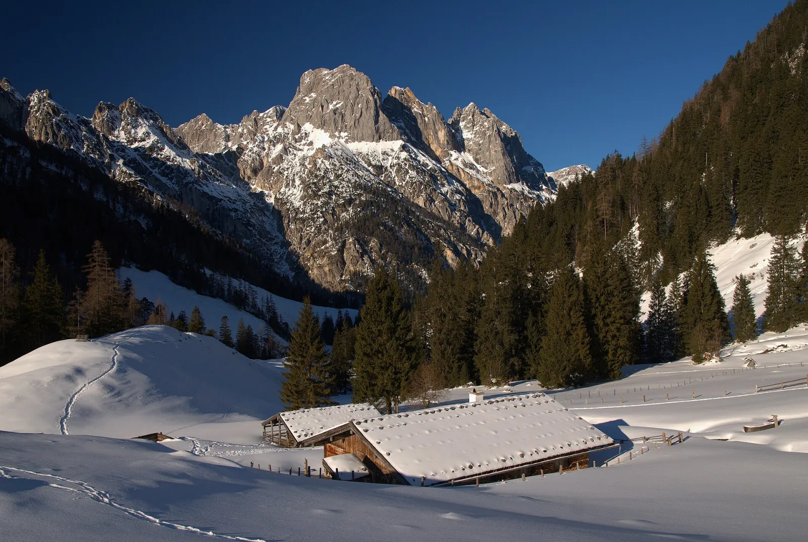 The snow-covered Bindalm in Berchtesgaden National Park, with its alpine huts, behind it the rock peaks of the Mühlsturzhörner under a deep blue sky