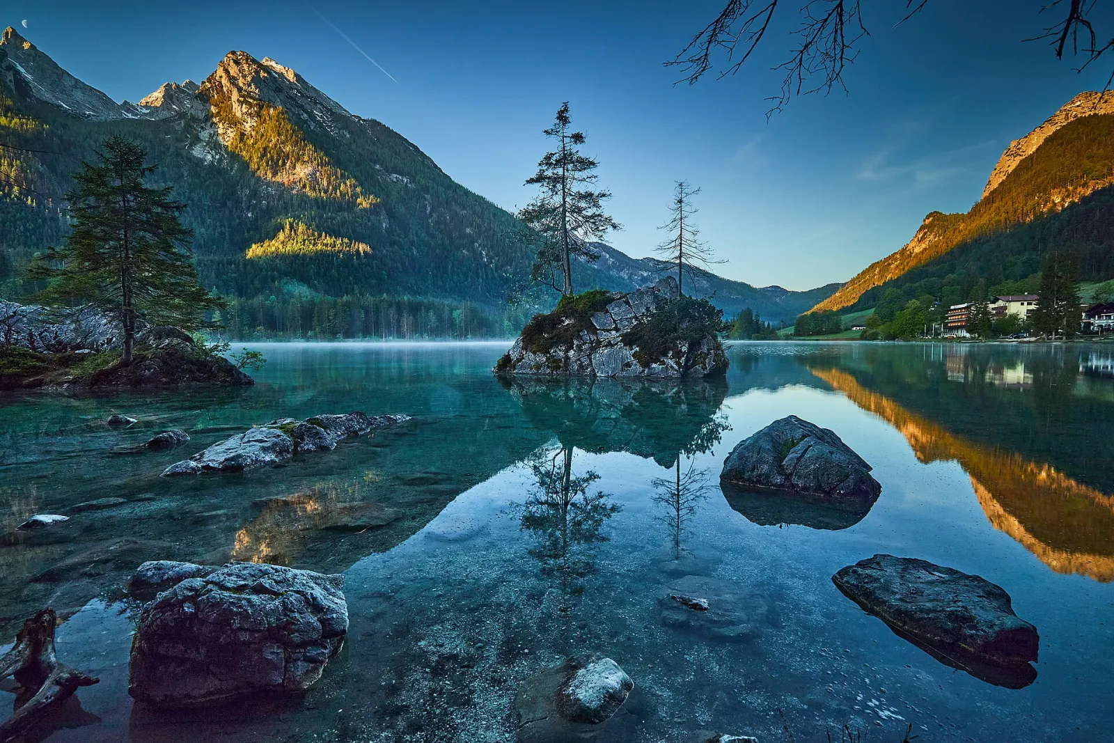 Dawn at Lake Hintersee: rocky islets with single trees reflected in the still water, the mountains behind in the first sunlight