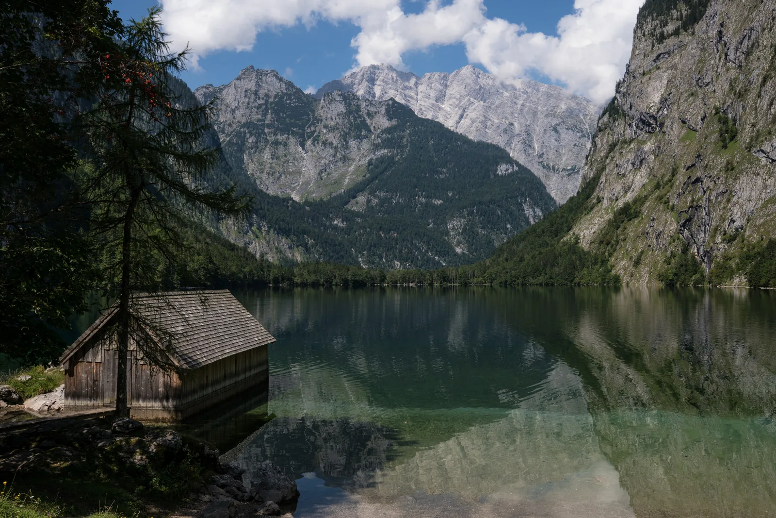 The Obersee in Berchtesgaden National Park reflects the surrounding rock walls, a wooden boathouse on the shore