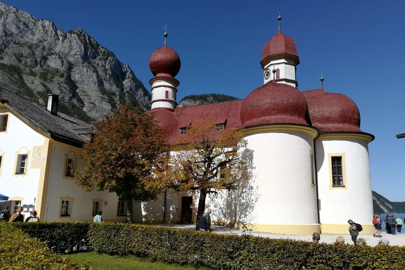 The church of St. Bartholomä in Berchtesgaden National Park, from the land side with its three apses, a tree in autumn leaves in front