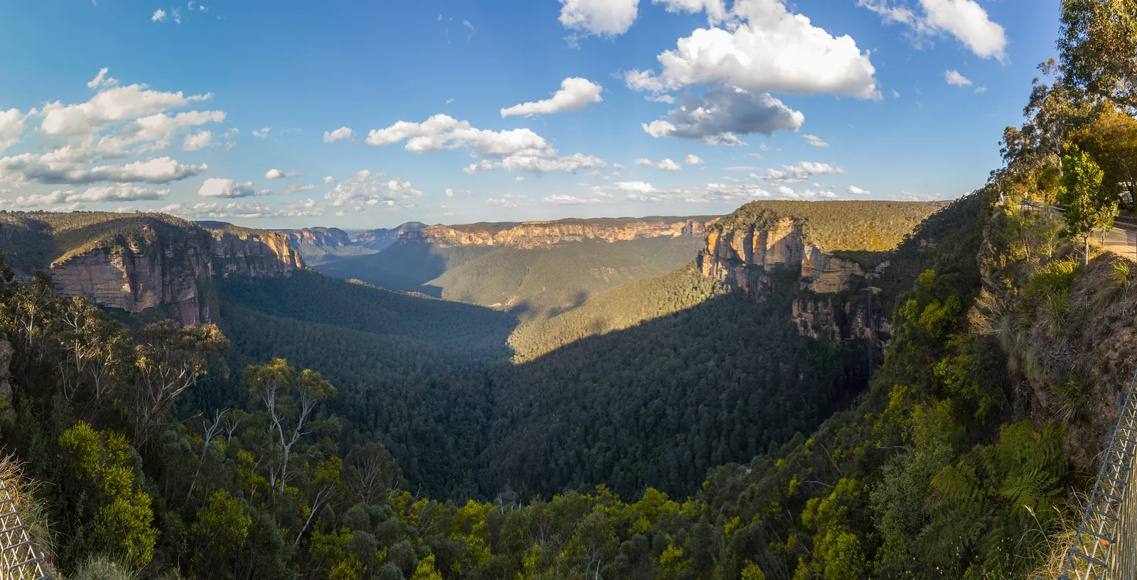 Panorama from Govetts Leap in Blue Mountains National Park: sandstone walls and the forested Grose Valley in the evening light, the lookout railing on the right