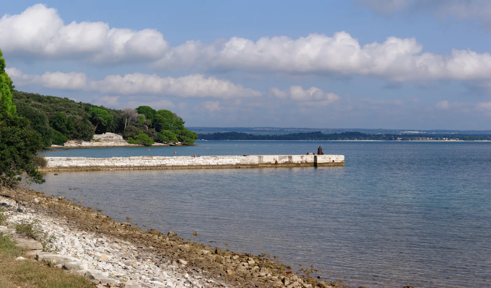 Stone jetty on the coast of Brijuni National Park, with a wooded shore and calm sea behind