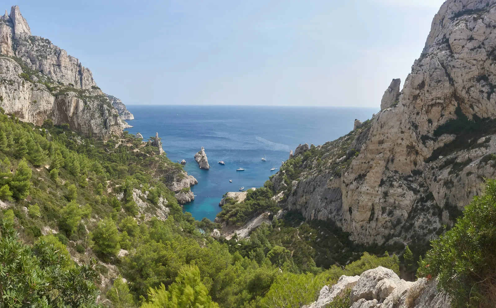 View from the path down to the Calanque de Sugiton in Calanques National Park: green slopes, limestone rocks and the islet of Le Torpilleur in turquoise water