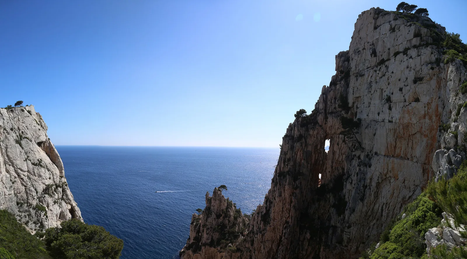 A limestone wall with a natural rock arch at the Calanque d’En-Vau in Calanques National Park, the open sea behind