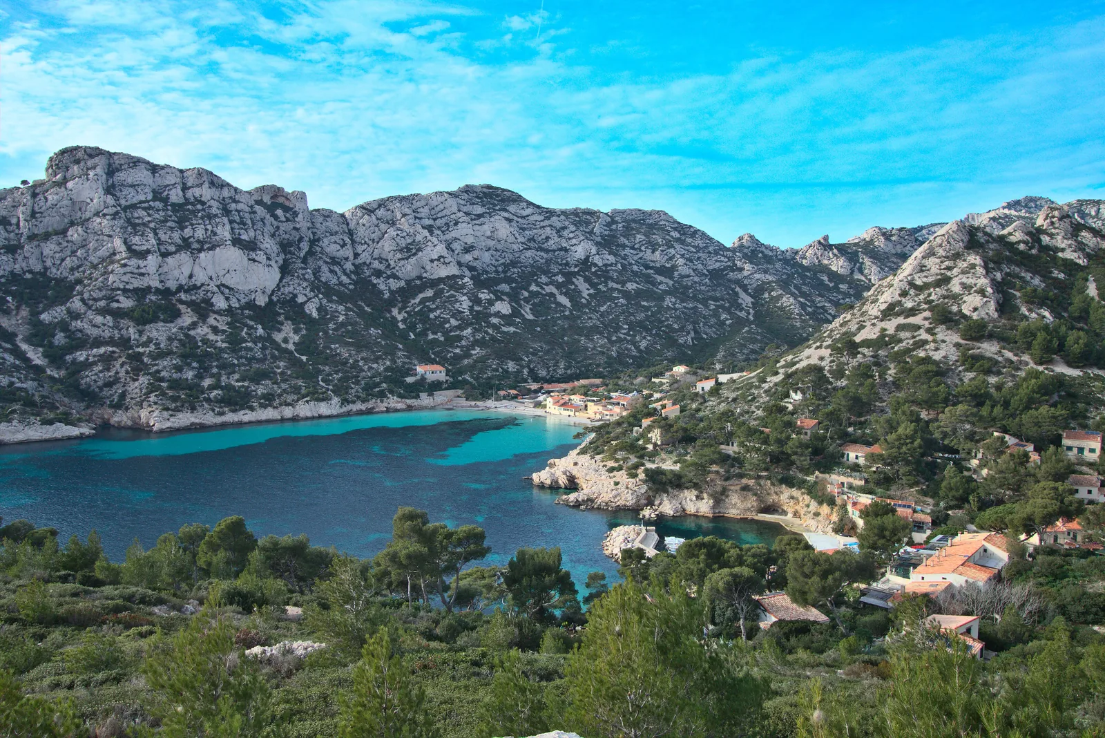 The Calanque de Sormiou in Calanques National Park seen from the Morgiou ridge: turquoise cove, beach, small houses and limestone hills