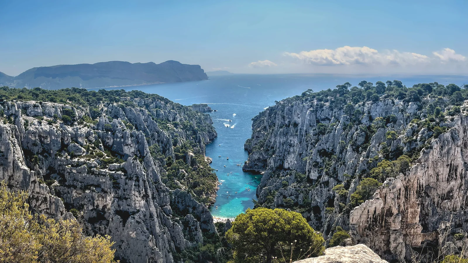 View from the Belvédère d’En-Vau in Calanques National Park: steep limestone walls with the turquoise cove of En-Vau between them, the sea and Cap Canaille behind