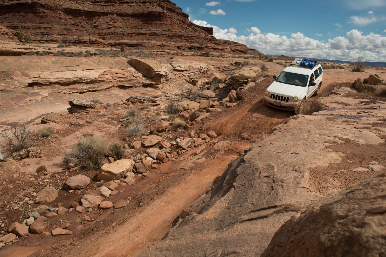 A white 4WD vehicle descends a steep, rock-lined ramp on the White Rim Road in Canyonlands National Park