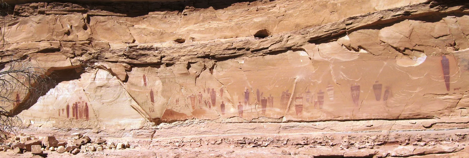 A row of dark red, life-size figures on a pale sandstone wall in Horseshoe Canyon, Canyonlands National Park