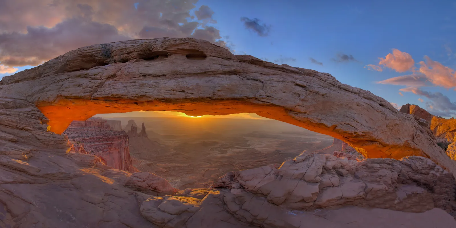 Mesa Arch in Canyonlands National Park, backlit at sunrise, the underside of the arch glowing orange above the canyon country