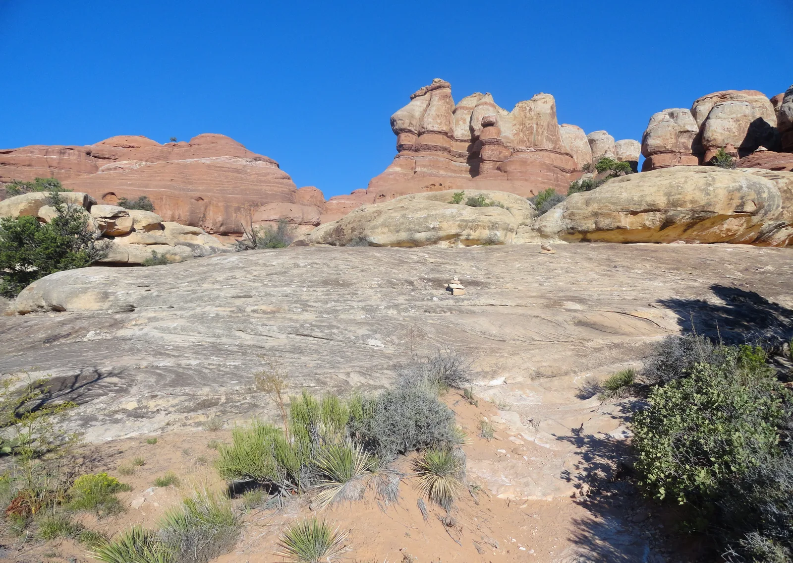 Bare sandstone in the foreground, behind it the banded rock spires of the Needles district in Canyonlands National Park under a blue sky