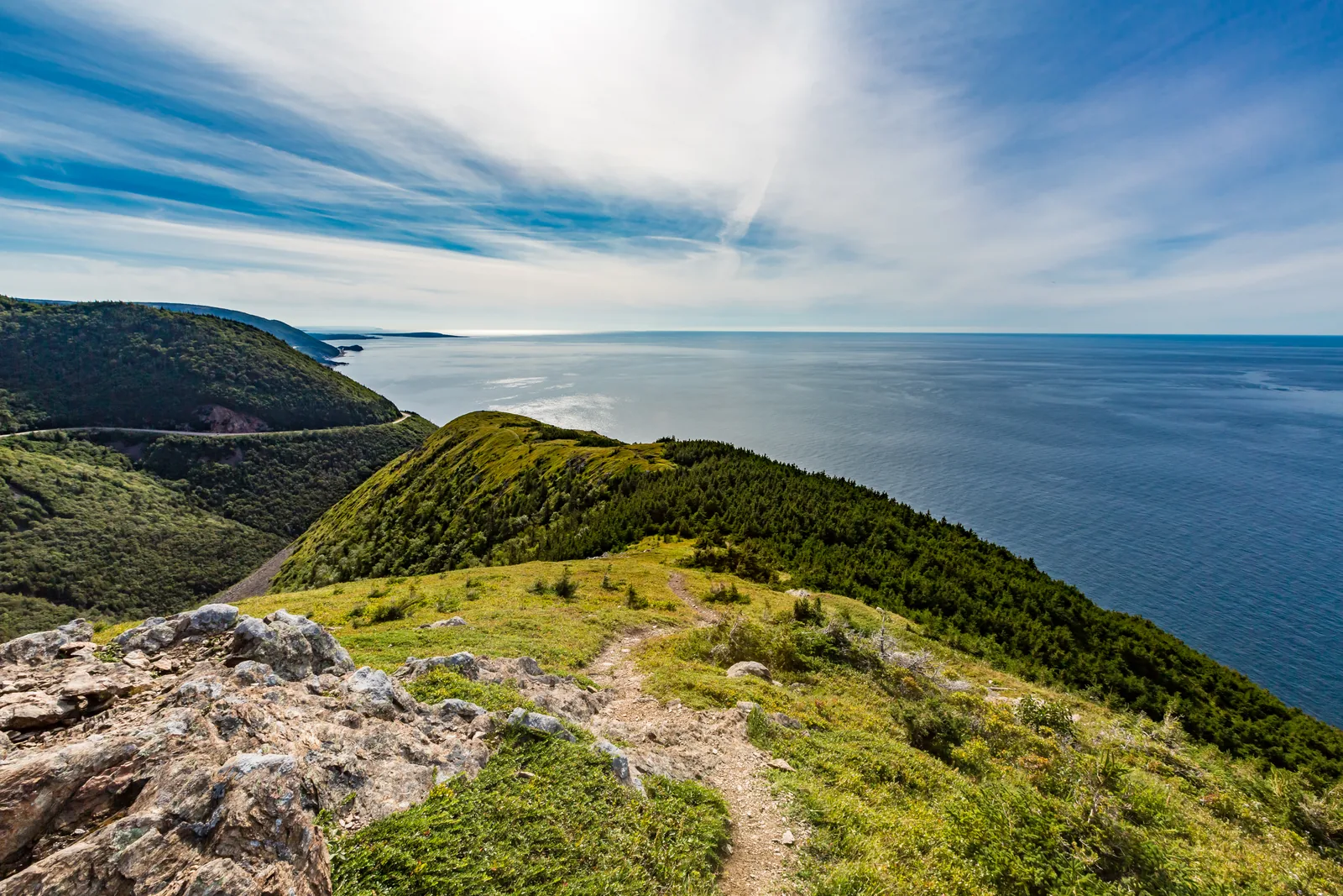 View from the end of the Skyline Trail in Cape Breton Highlands National Park: a green ridge drops to the sea, on the left the Cabot Trail winds along the coast