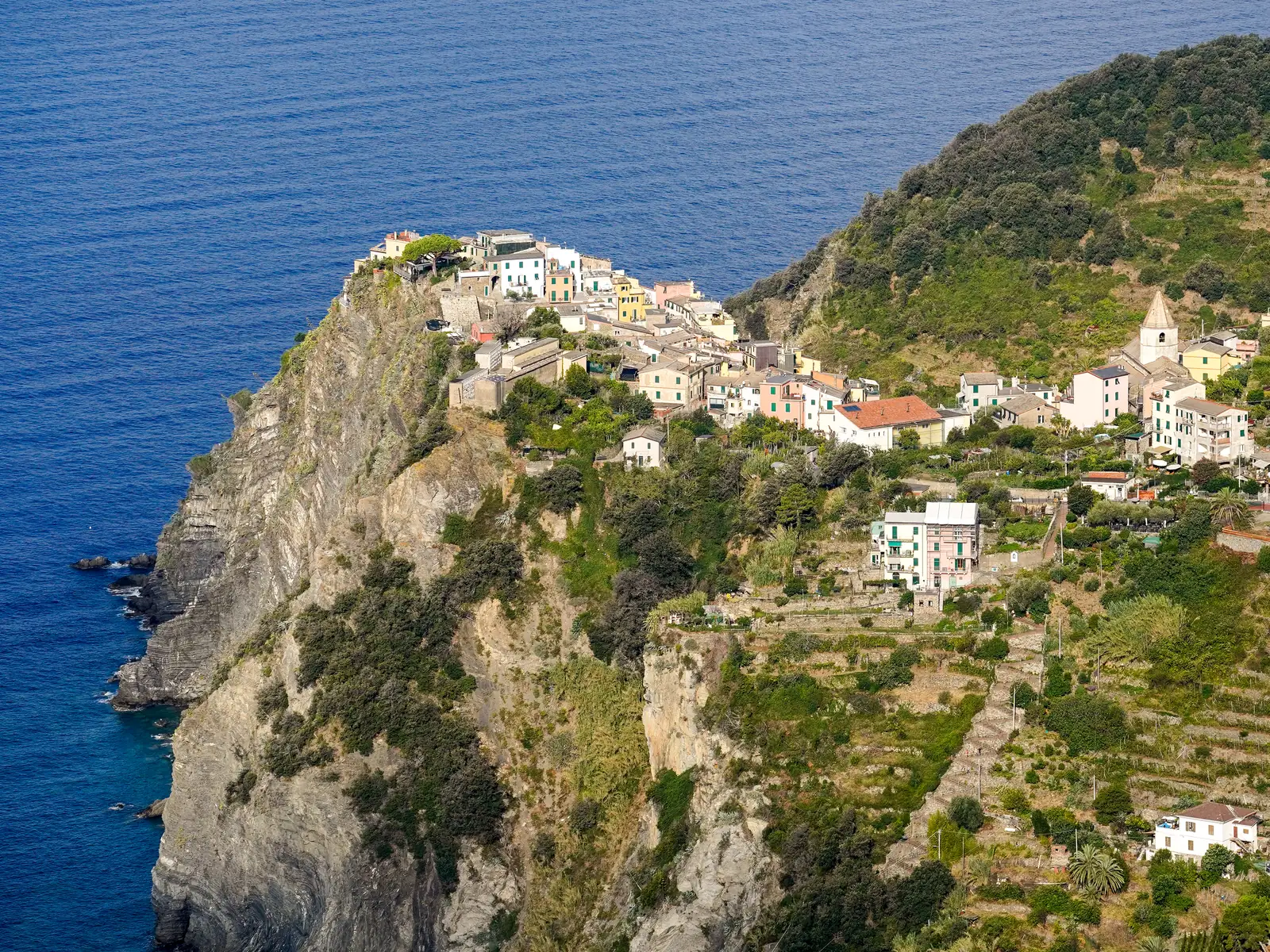 Corniglia in Cinque Terre National Park on its rocky promontory above the sea, with vineyard terraces on the slope to the right