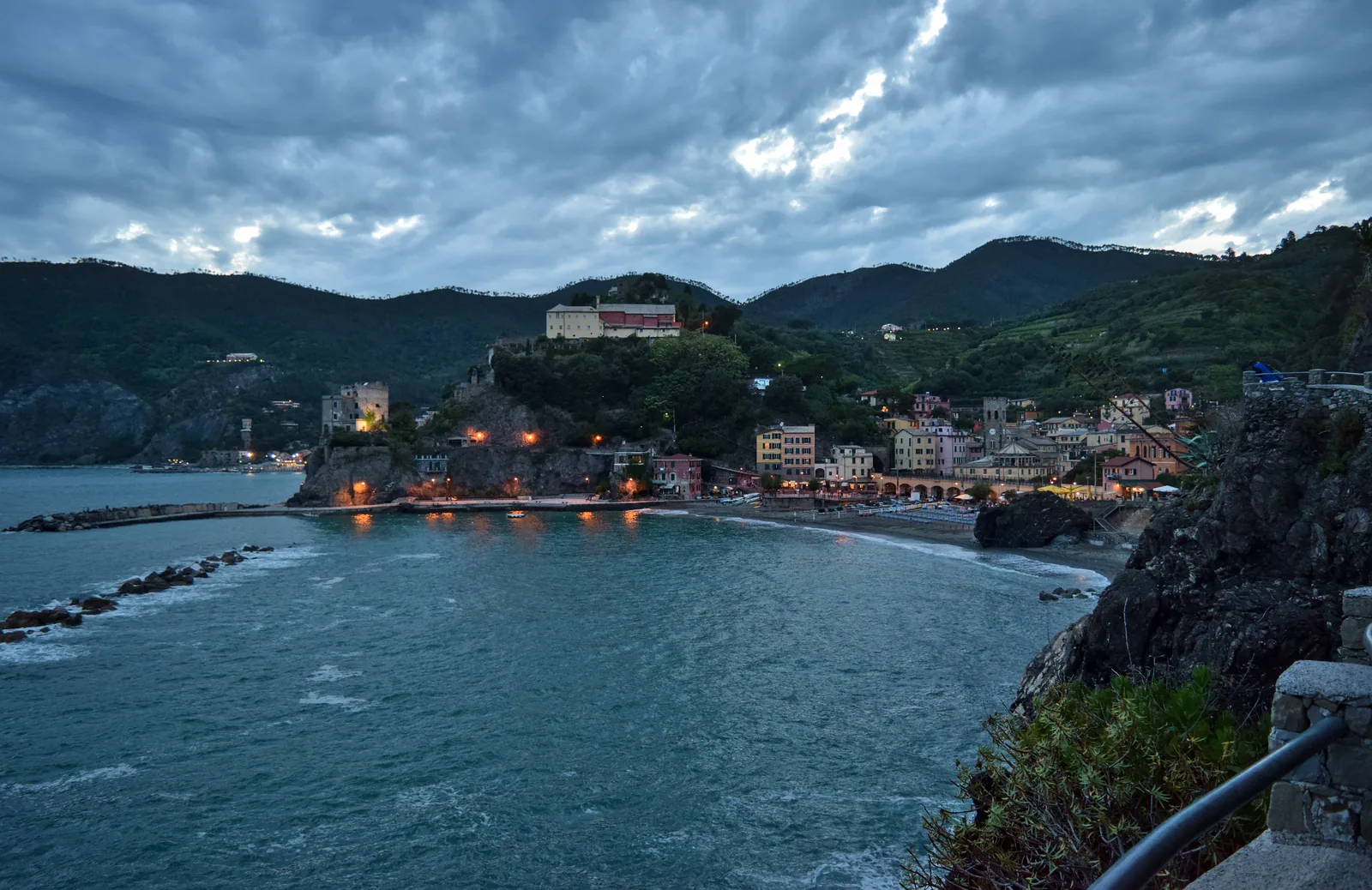 Dusk over the harbour of Monterosso al Mare in Cinque Terre National Park, with the lights of the village and wooded hills behind