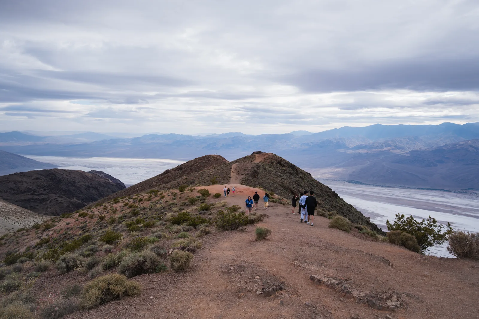 Visitors walk along a path on the ridge at Dantes View in Death Valley National Park, with the white salt flat of the valley far below