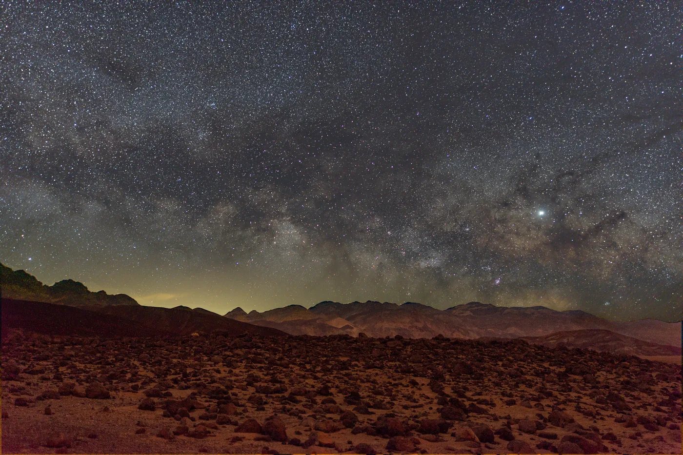The Milky Way above a stony plain and dark mountain ranges in Death Valley National Park