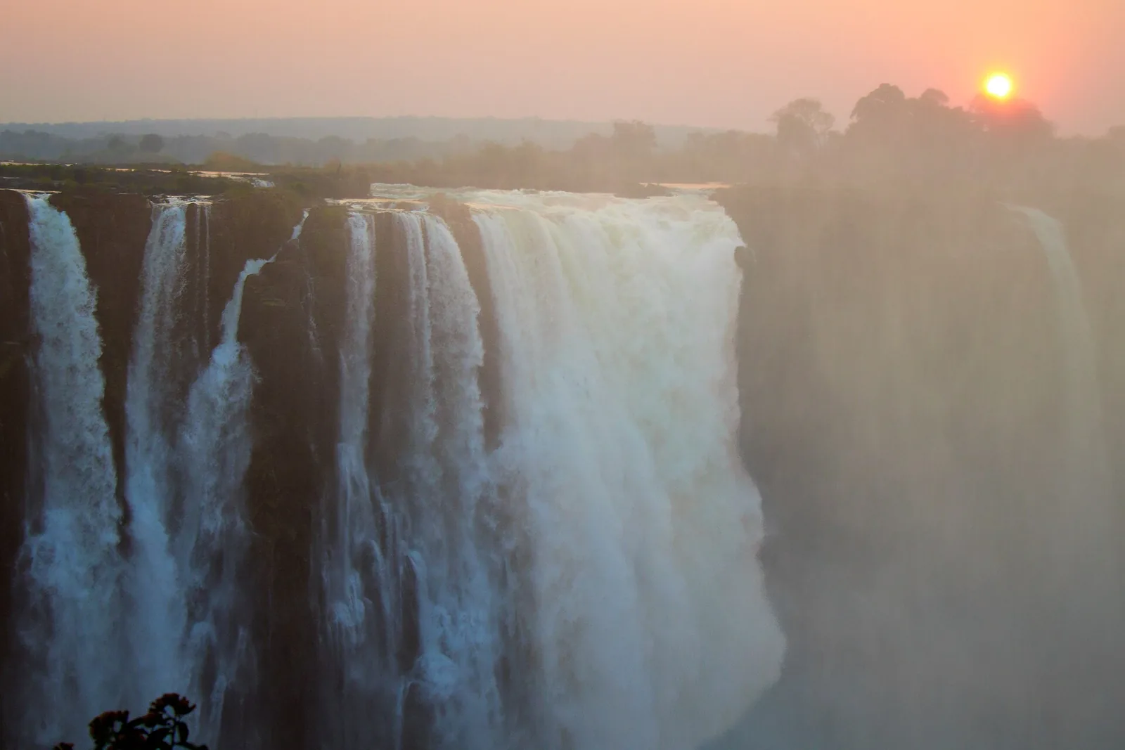 Victoria Falls in the evening light, water pouring over the edge and the spray glowing against the low sun