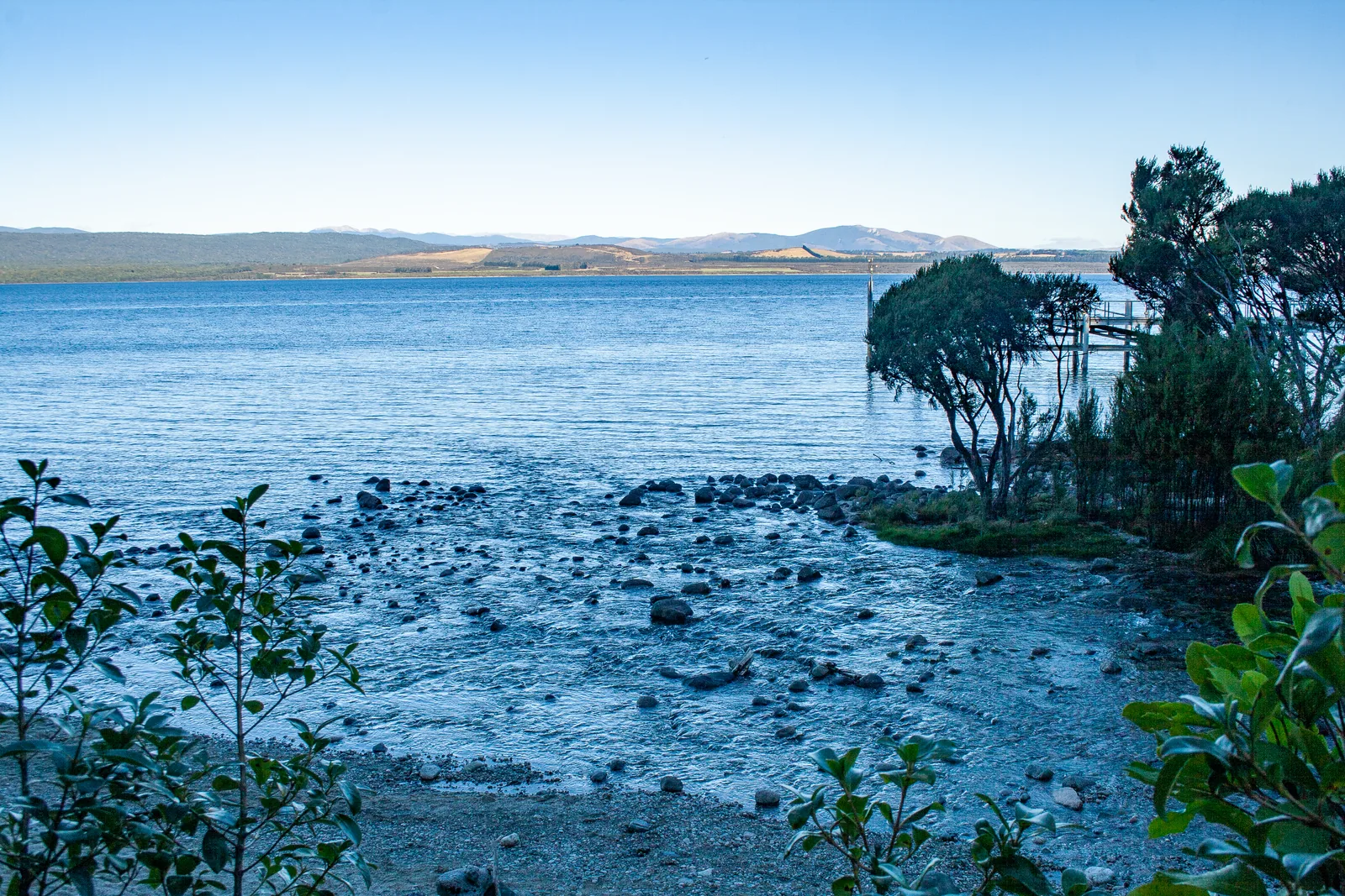 Stony shore of Lake Te Anau at the glowworm caves in Fiordland National Park, with the flat eastern shore of the lake in the background