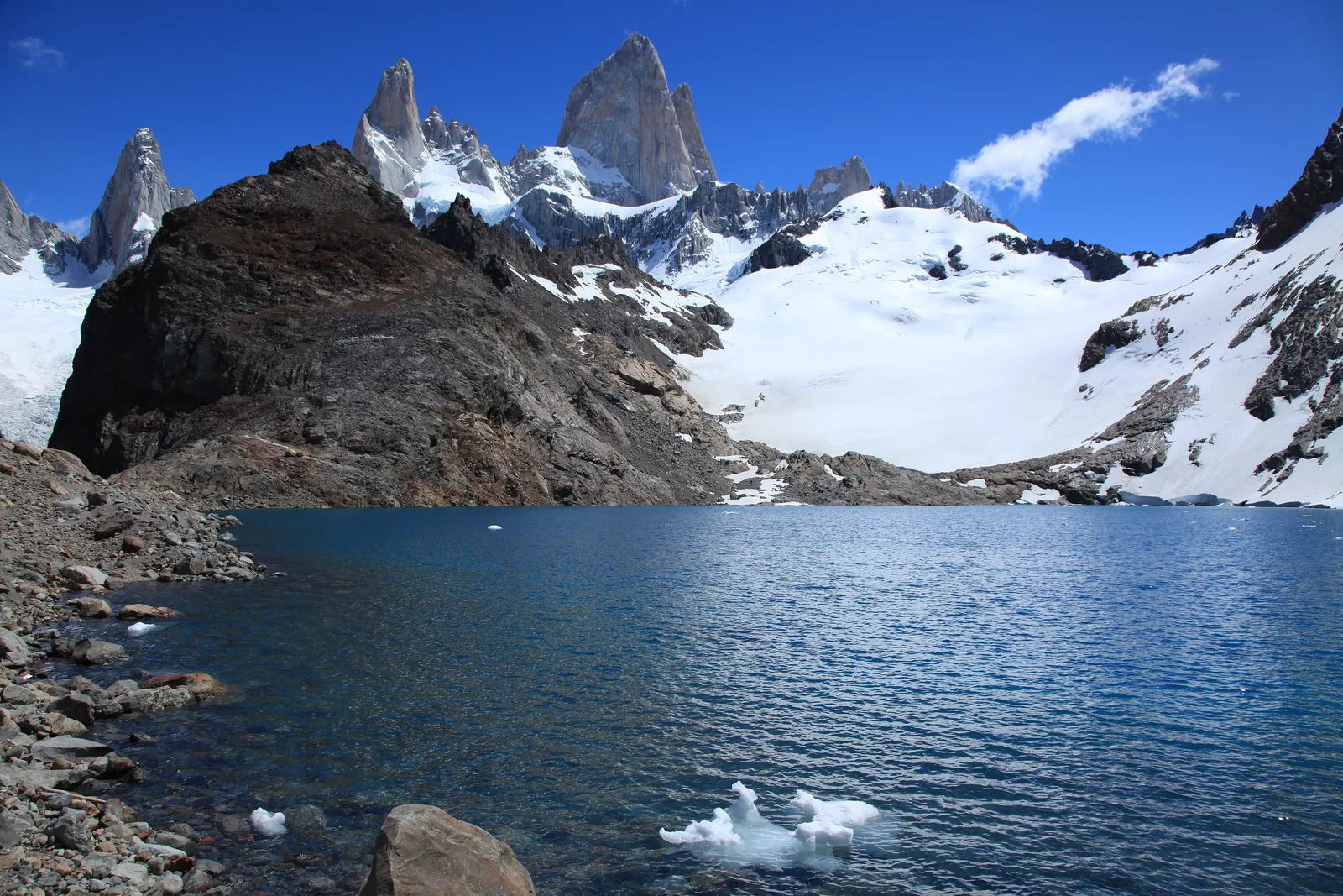 Fitz Roy in Los Glaciares National Park above Laguna de los Tres, a dark rocky ridge and snowfields in front under a blue sky