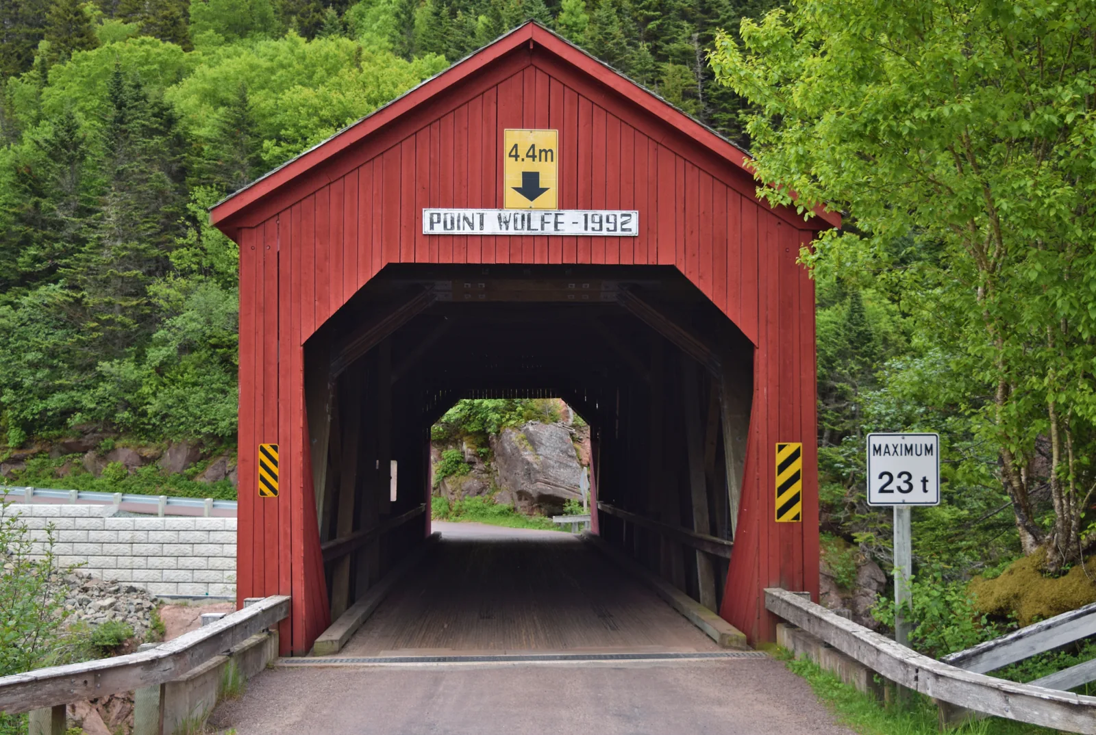 The red covered wooden bridge at Point Wolfe in Fundy National Park from the front, with height and load limits on the portal, dense forest all around