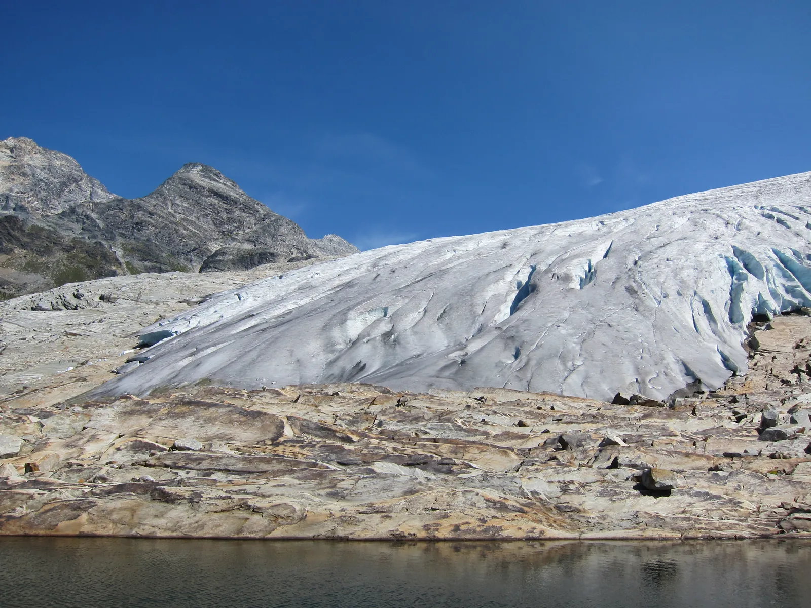 The tongue of the Illecillewaet Glacier in Glacier National Park in Canada ends above polished bare rock, a small glacial lake in front