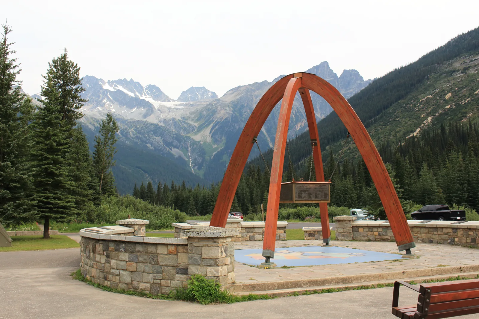 Wooden arch of the summit monument at Rogers Pass in Glacier National Park in Canada, forested slopes and the glaciers of the Hermit Range behind