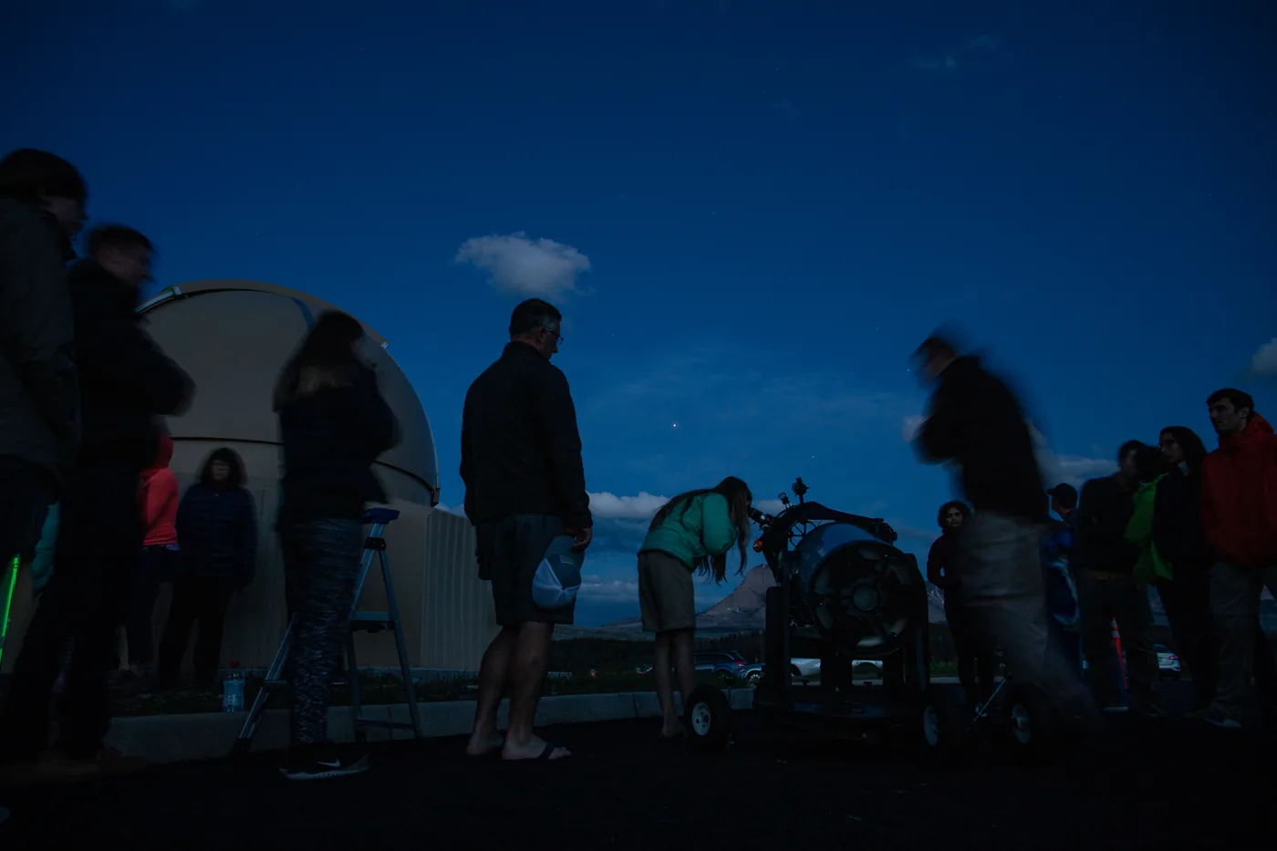 Visitors at an astronomy programme by the dome of the Dusty Star Observatory at the St. Mary Visitor Center in Glacier National Park, a telescope in front of mountain silhouettes in the last evening light