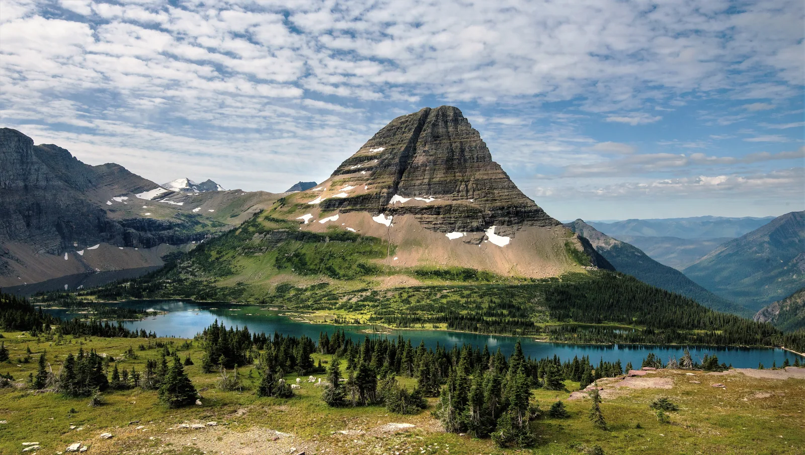 The turquoise Hidden Lake in Glacier National Park, Montana, below the pyramid-shaped Bearhat Mountain, with alpine meadows and conifers in the foreground
