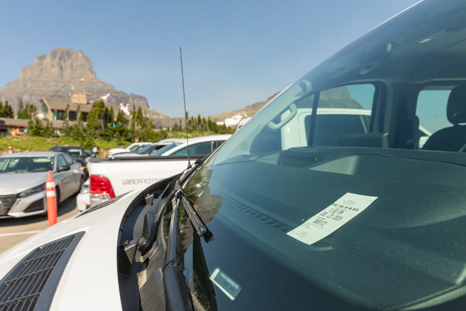 A parking permit behind the windscreen of a car in the full car park at Logan Pass in Glacier National Park, Montana, with the visitor centre and mountains behind