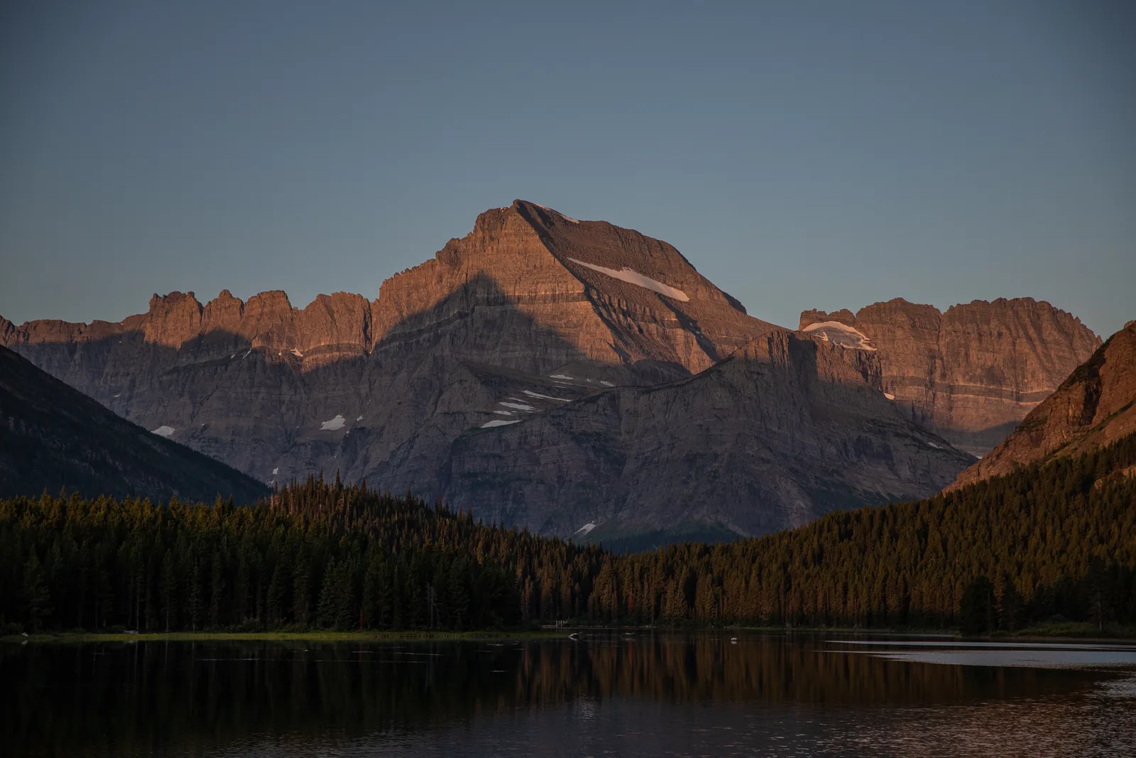 Sunrise over Swiftcurrent Lake, with the mountainsides opposite glowing red, seen from the Many Glacier Hotel