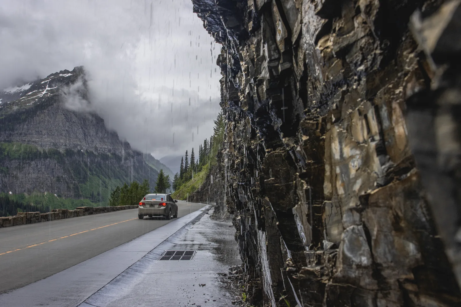 Water pours from the Weeping Wall straight onto the wet surface of the Going-to-the-Sun Road in Glacier National Park, Montana, as a car drives past