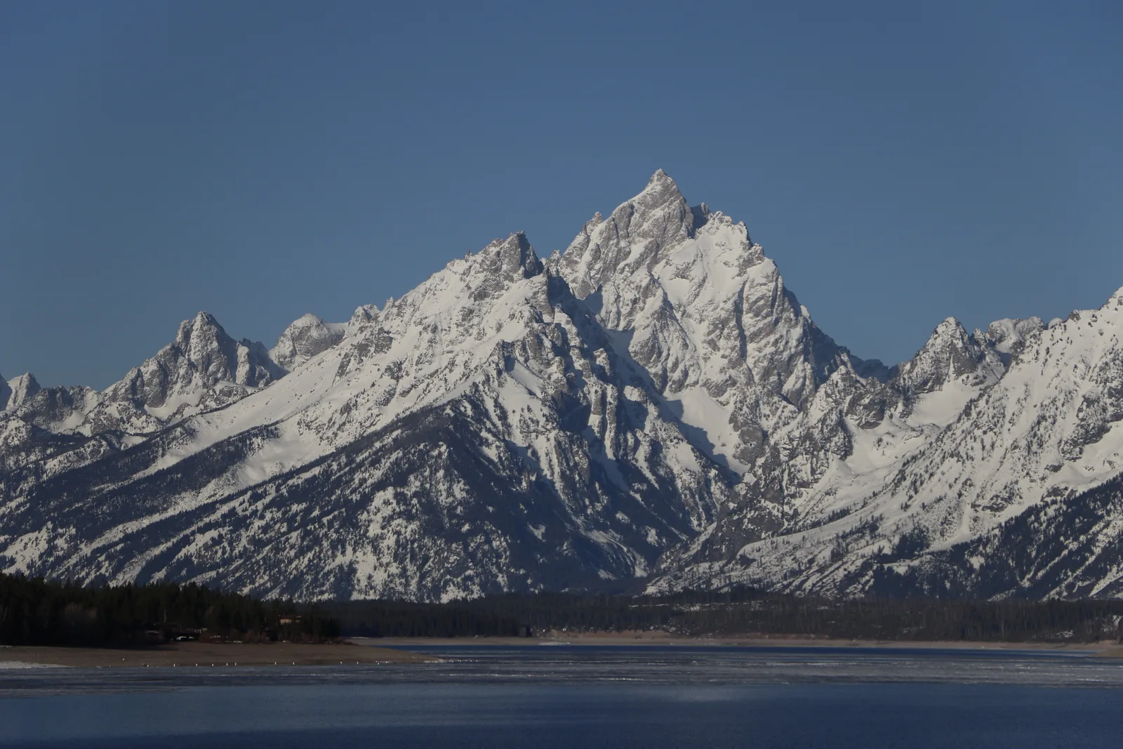 The snow-covered Cathedral Group in Grand Teton National Park above a thawing Jackson Lake with ice floes in the foreground