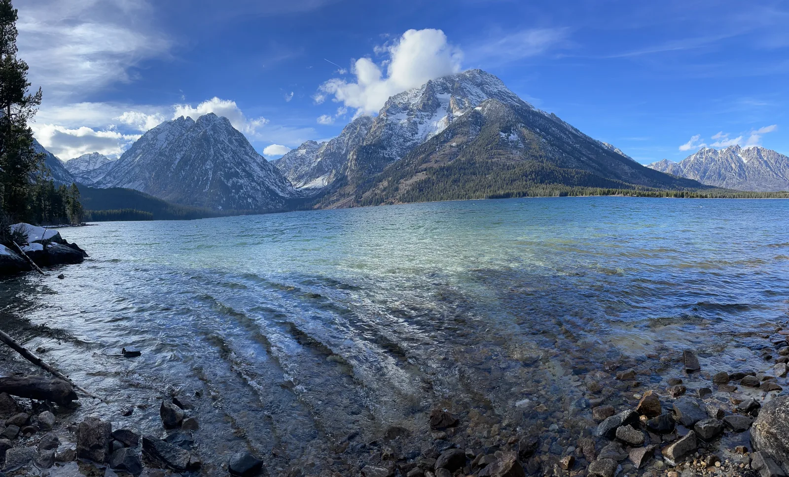 Clear shallow water on the shore of Jackson Lake in Grand Teton National Park, with the Teton Range under a blue sky behind